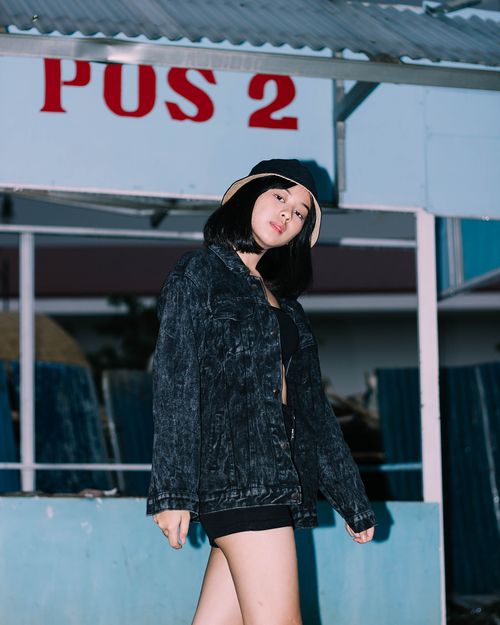 Free Stylish woman wearing denim jacket and bucket hat posing outdoors in urban setting. Stock Photo