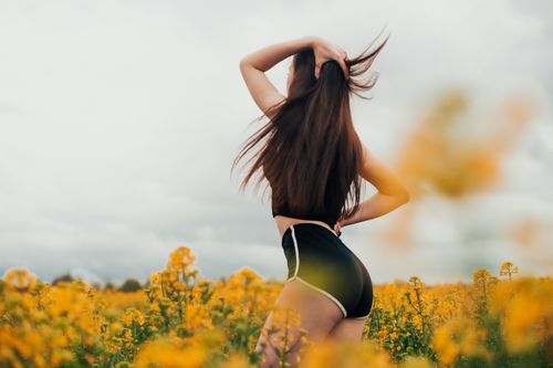 Free A woman in a black outfit enjoying a vibrant field of yellow flowers with a gentle breeze. Stock Photo