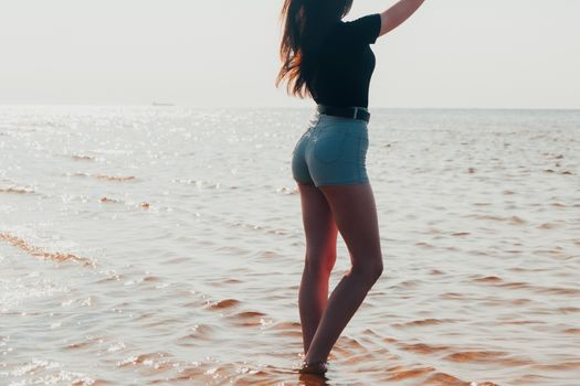 A woman wearing denim shorts stands in the ocean on a sunny day.