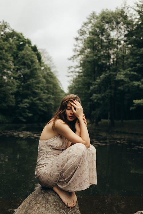 Photo of a Woman Sitting on a Rock while Her Hand is on Her Face