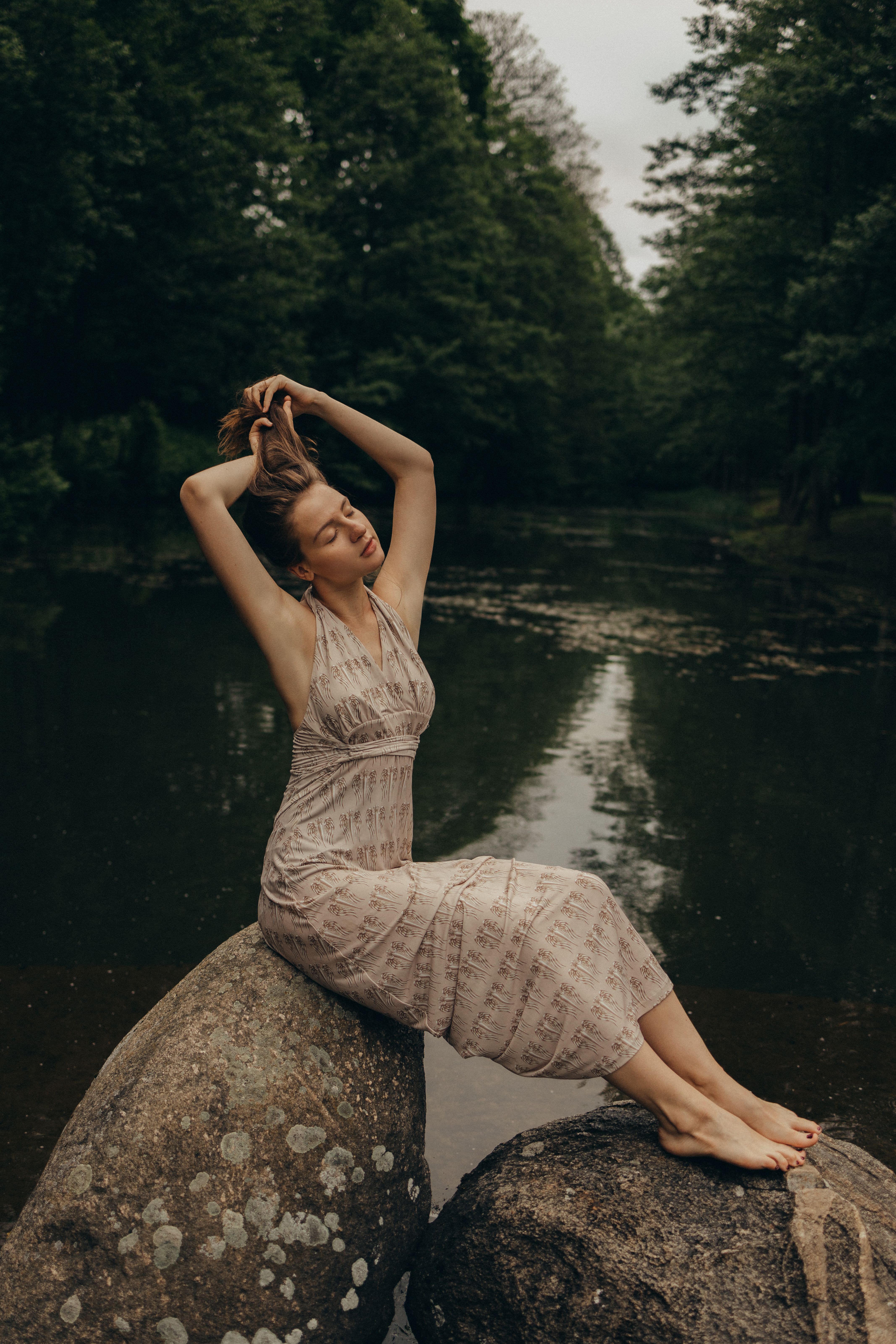 一位穿着连衣裙的白人妇女，在湖边岩石上优雅地摆着姿势，周围是宁静的自然环境