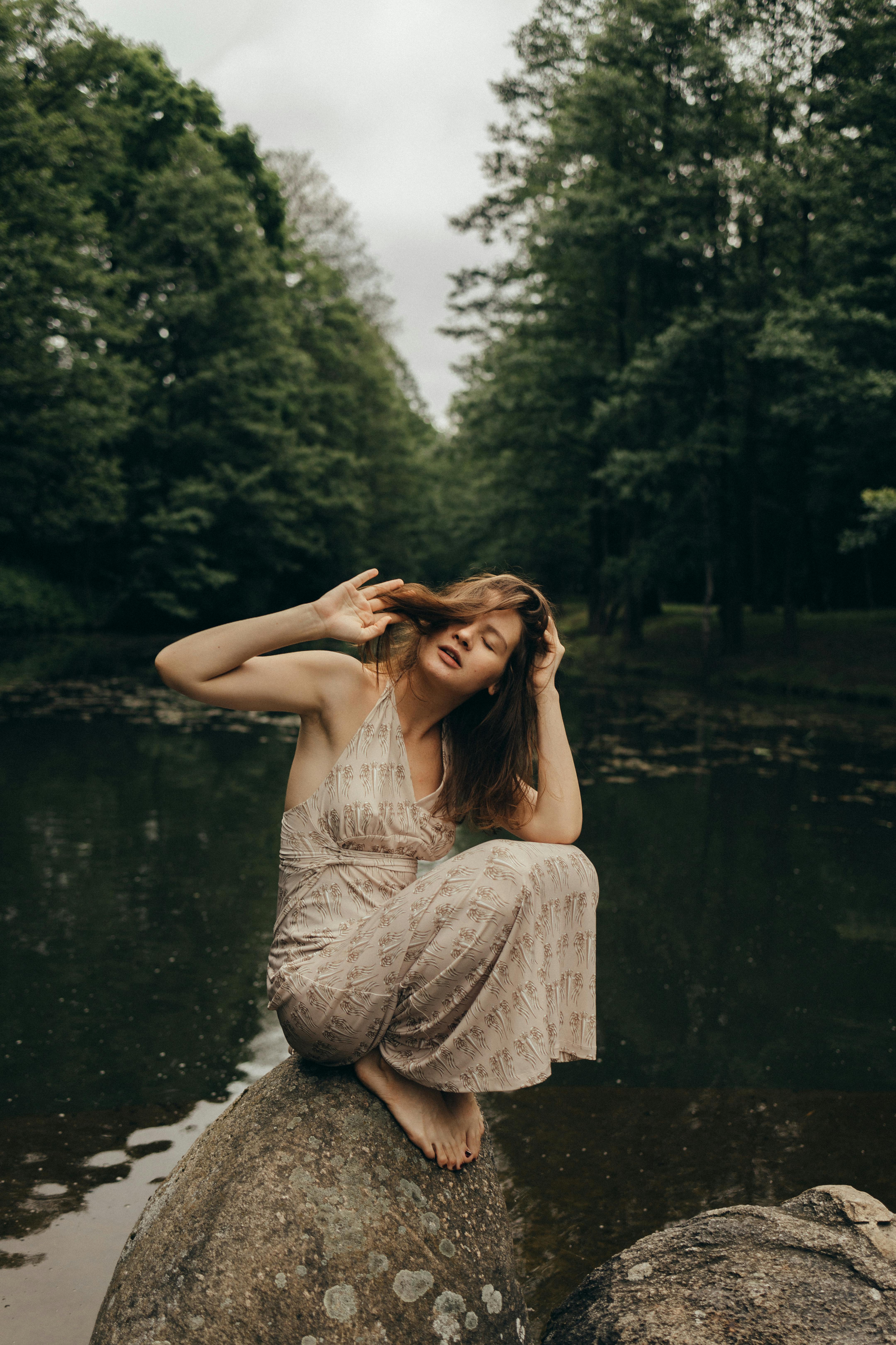 一位穿着蕾丝连衣裙的女人安静地坐在森林池塘边的岩石上