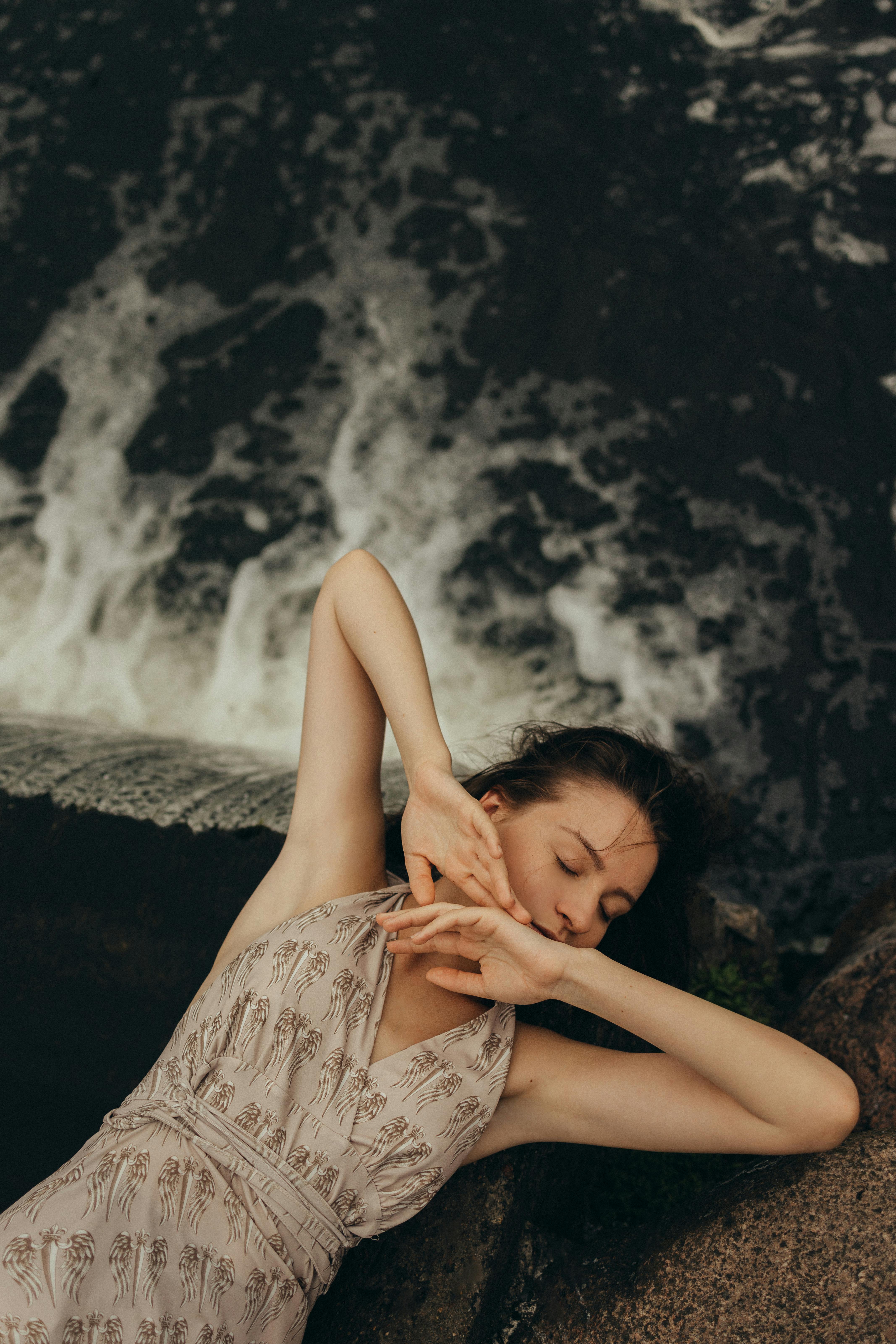 一位女子静静地躺在瀑布旁，闭着眼睛，尽显宁静与自然