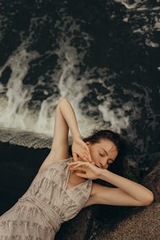 一位女子静静地躺在瀑布旁，闭着眼睛，尽显宁静与自然