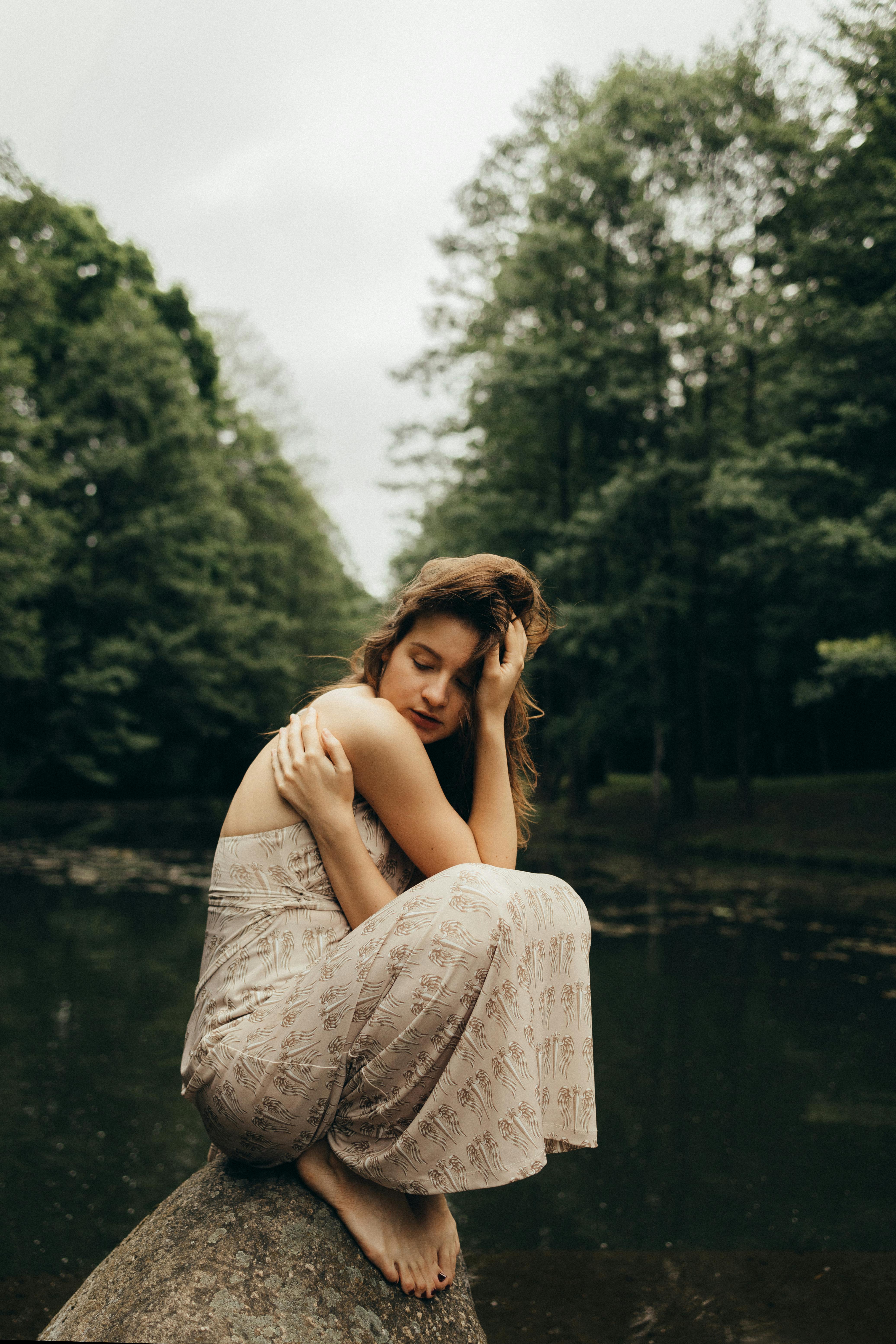 一位身着连衣裙的女子在森林的河边冥想，营造出宁静的氛围