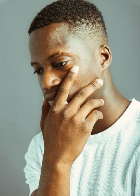 Portrait of a thoughtful Black man wearing white shirt, touching face, deep in reflection.