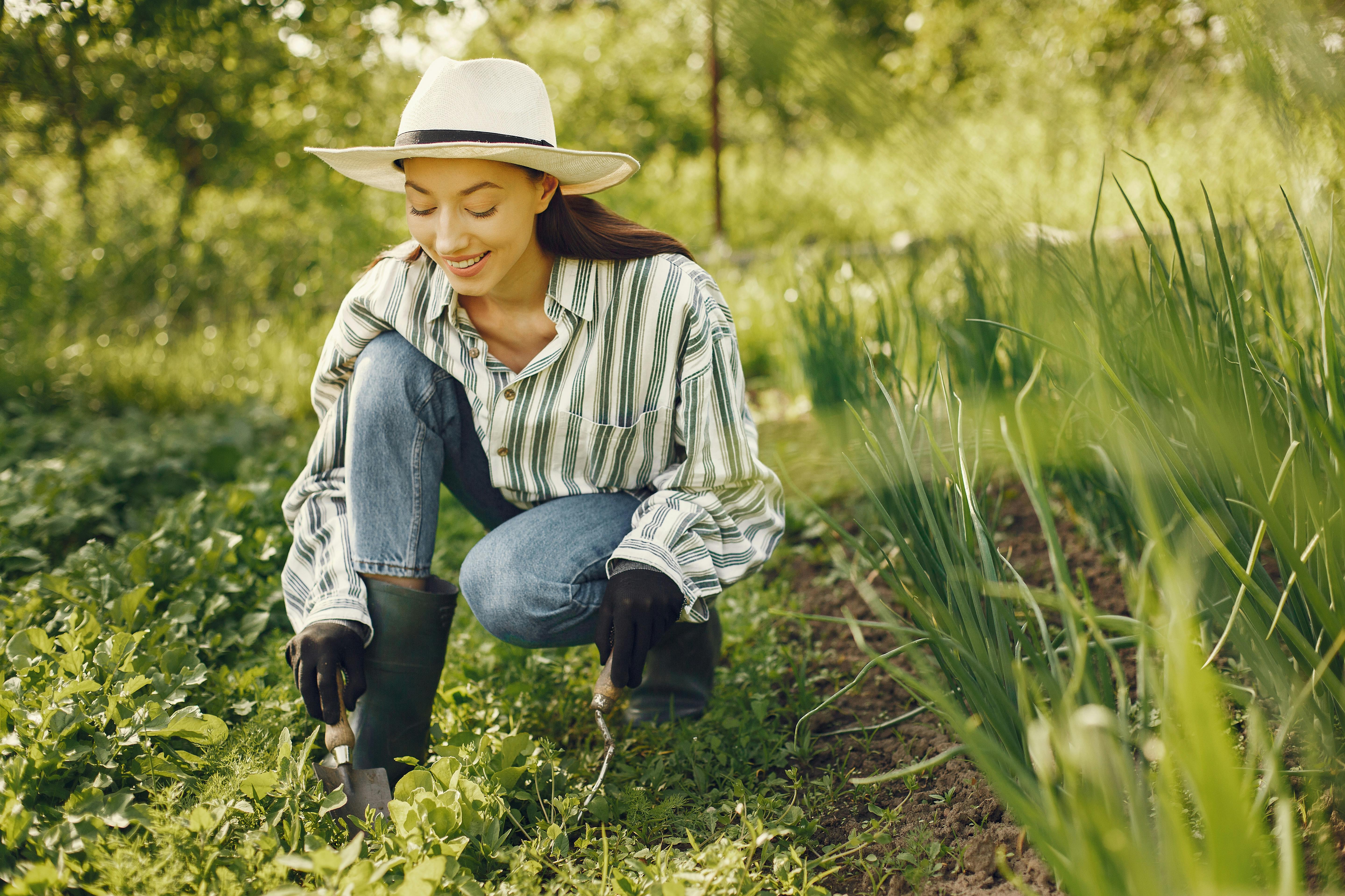 A woman joyfully tending to a garden, surrounded by lush greenery on a sunny day.