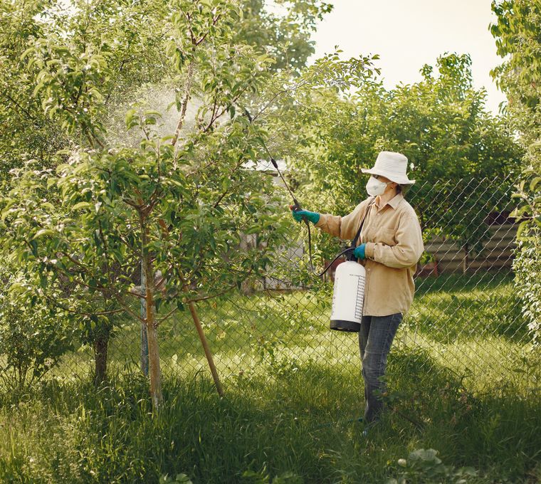 A pest control technician treating the exterior of a Long Branch home