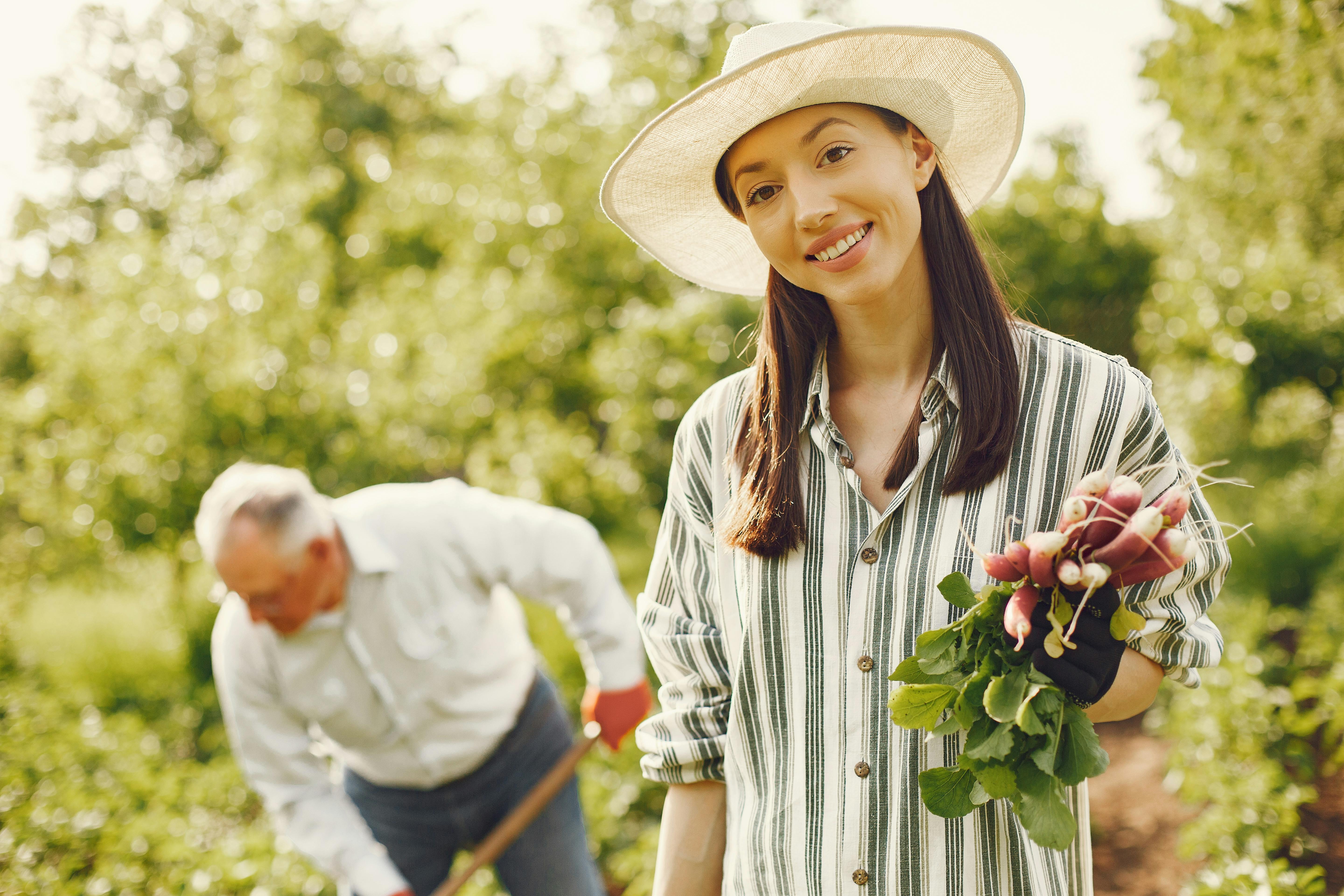 A cheerful woman holding freshly harvested radishes in a sunny garden.