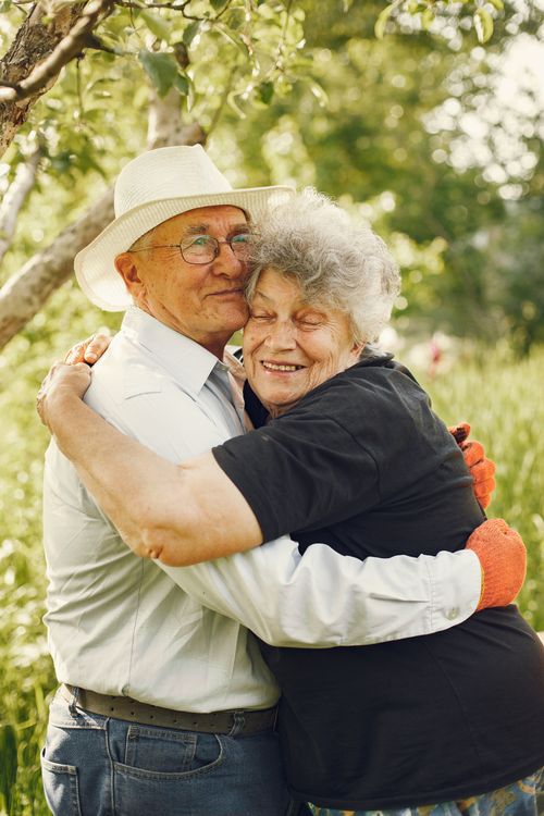 Free Happy senior couple hugging in a lush green garden, enjoying a sunny day. Stock Photo