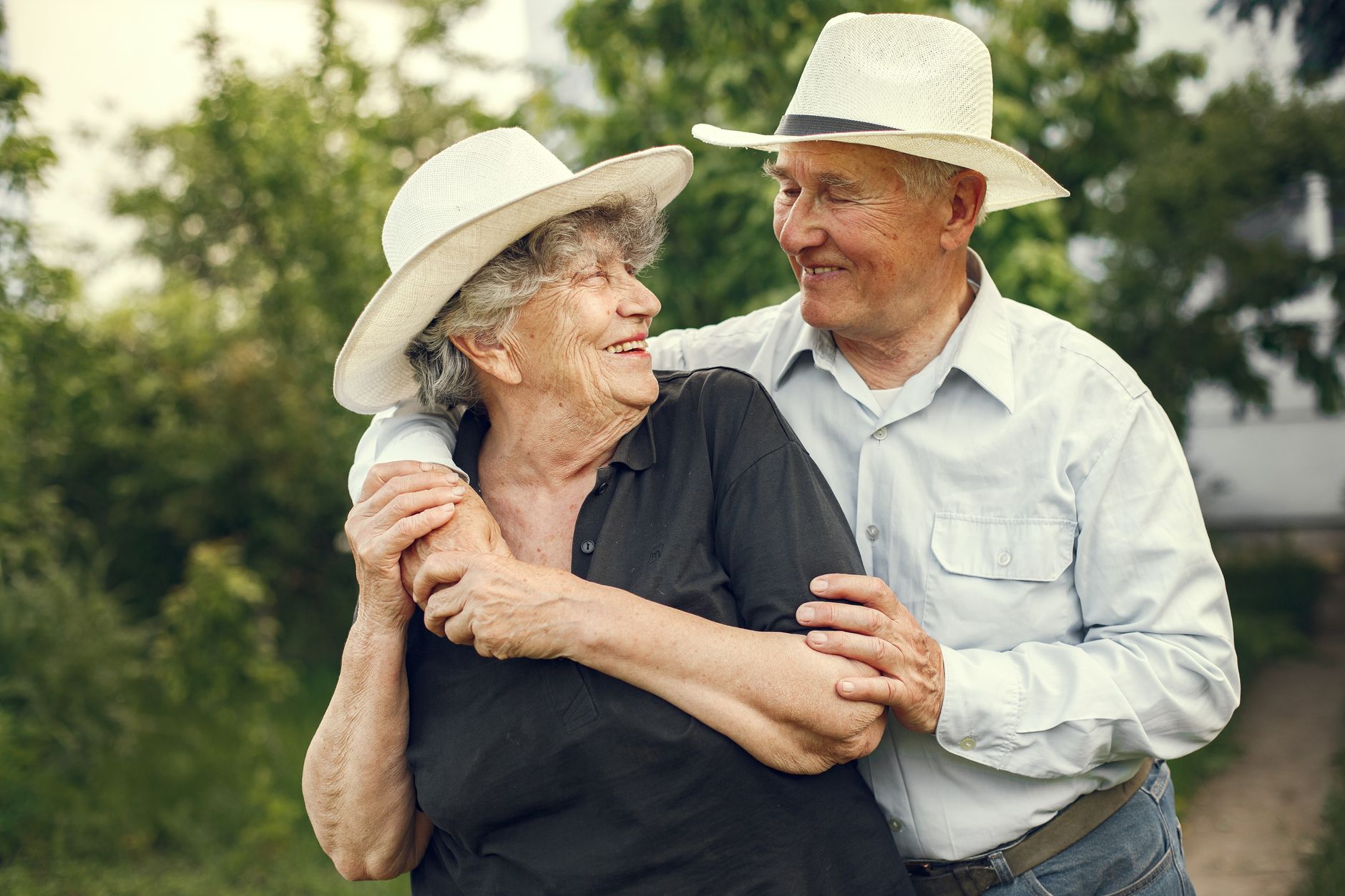 Happy senior couple wearing hats, sharing a joyful moment outdoors, embracing and smiling.