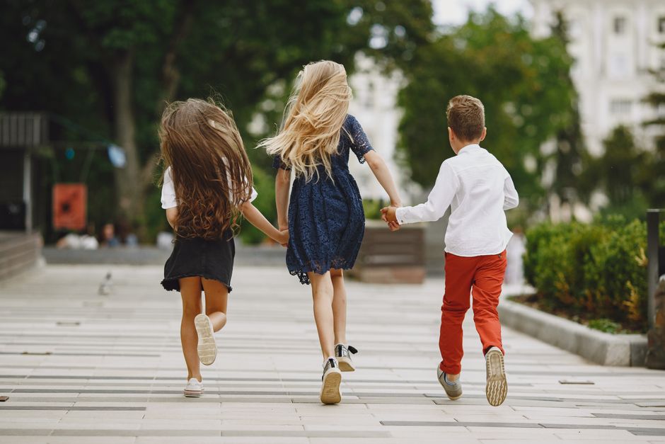 Tres niños corriendo de la mano al aire libre, ejemplificando amistad y alegría.