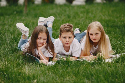 Free Three children lying on the grass writing in notebooks on a sunny day. Stock Photo