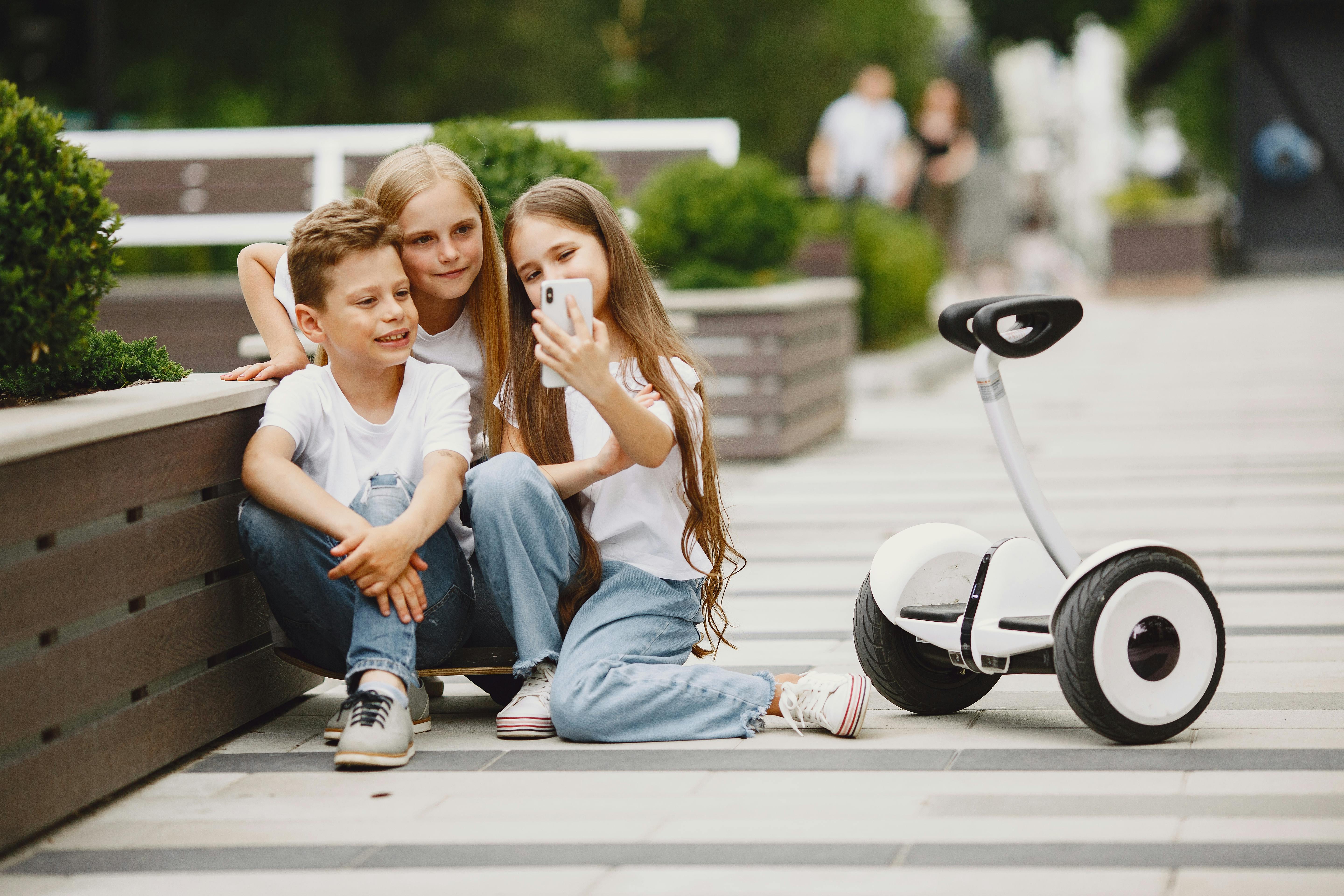 kids sitting and taking selfie next to balancing scooter