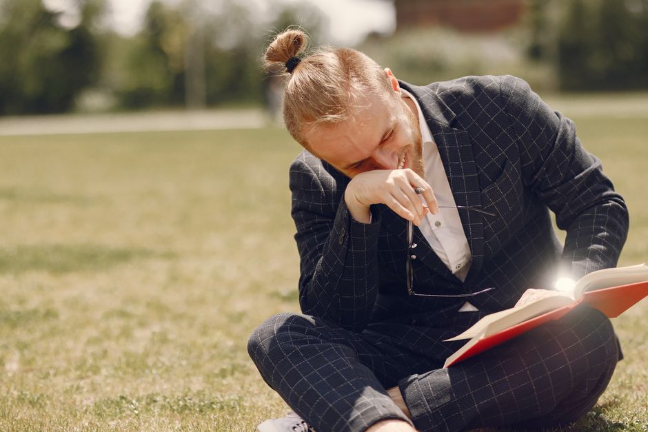 A businessman in a suit enjoying a sunny day outdoors while reading a book, conveying leisure and happiness. A businessman in a suit enjoying a sunny day outdoors while reading a book, conveying leisure and happiness.