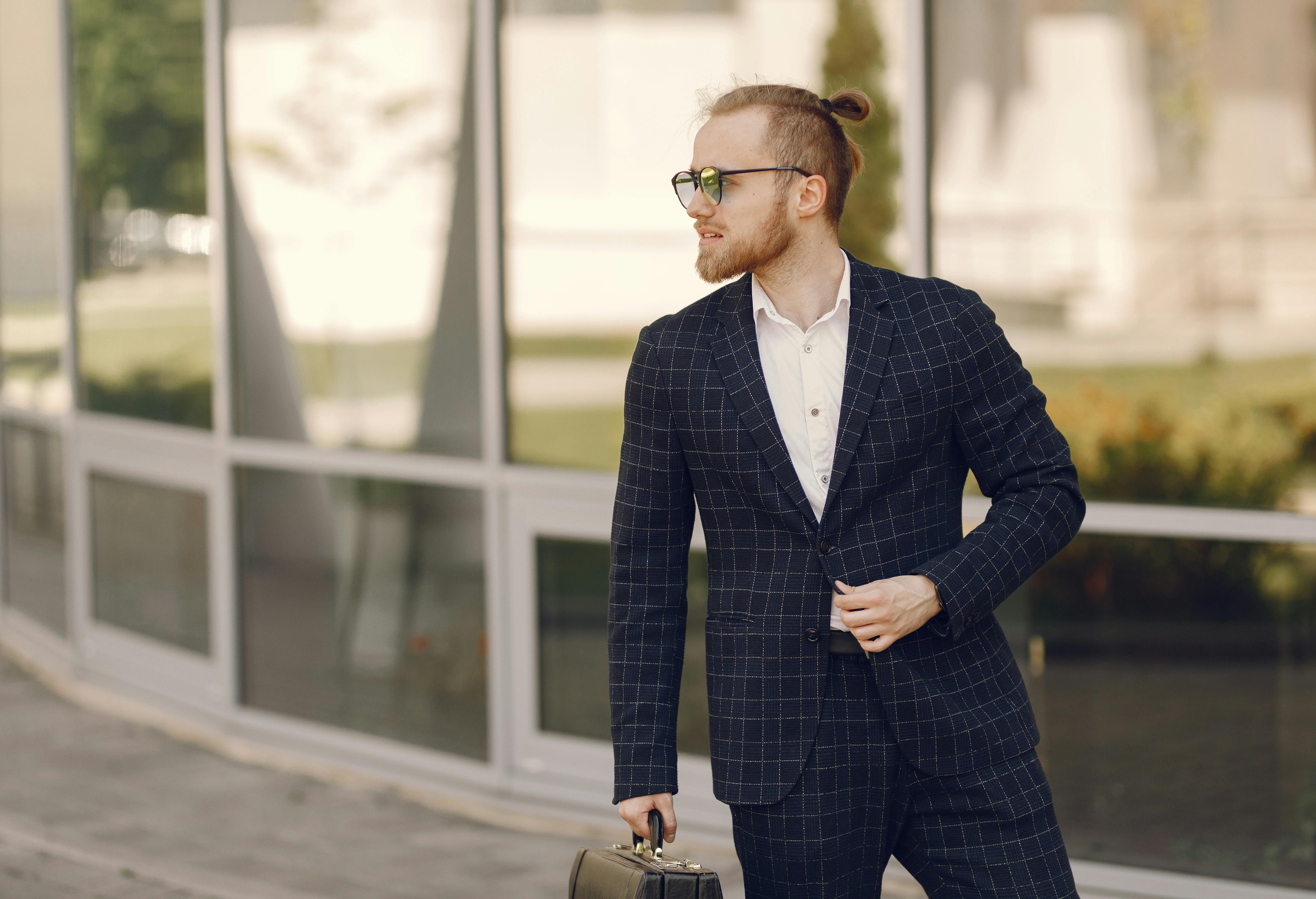 Businessman with man bun and briefcase outside modern building.