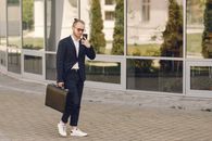 Man in Black Suit Jacket and Black Pants Wearing Black Sunglasses Standing Near Glass Window during