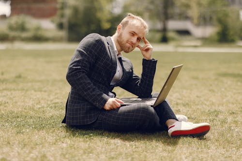 Man Sitting On Green Grass Field Holding A Laptop