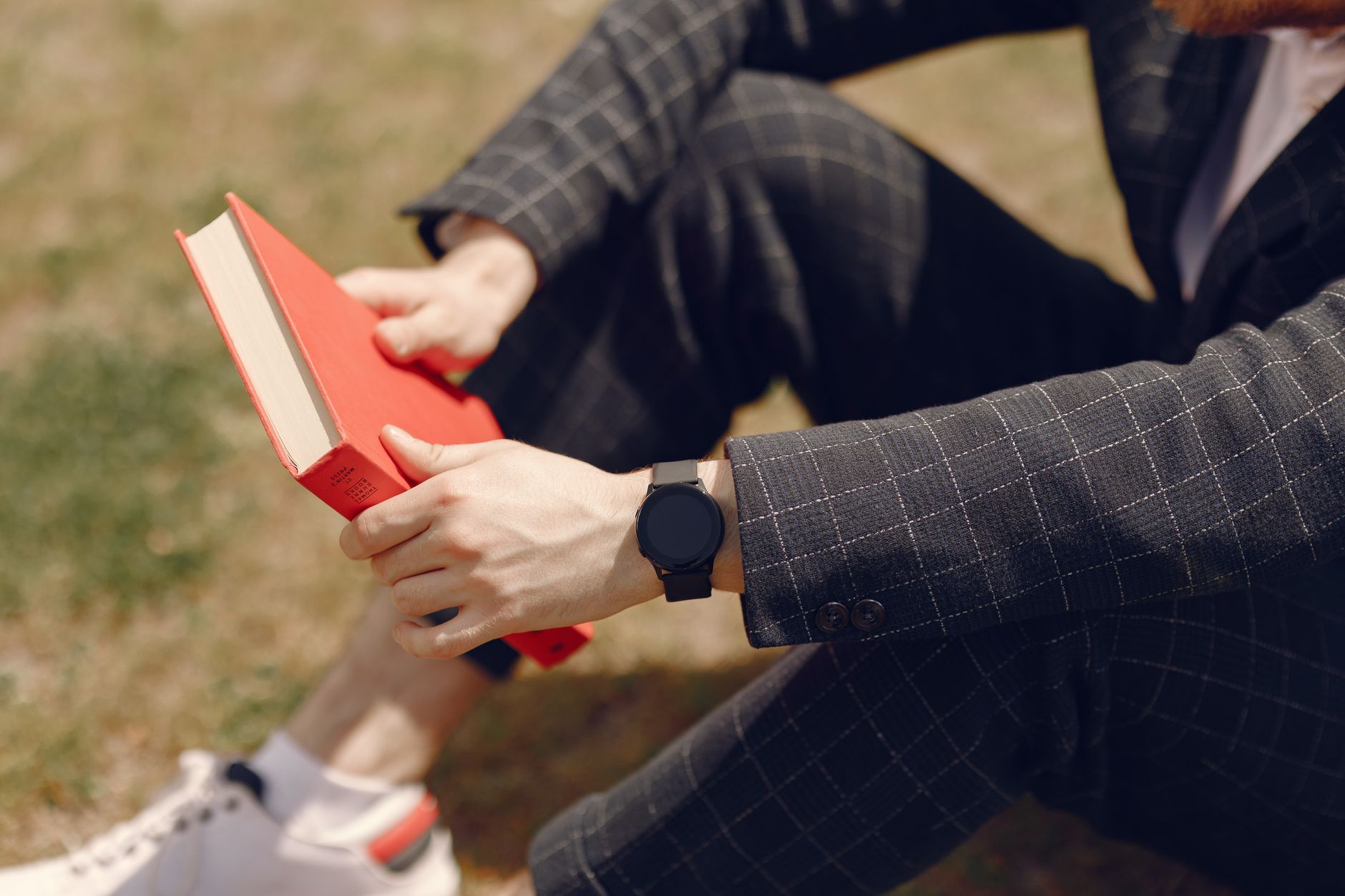 Stylish man in suit reading a red book outdoors on a sunny day.