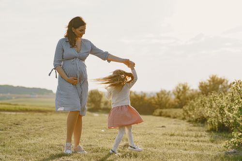 Free A pregnant mother and her daughter enjoying a joyful moment outdoors in the sunshine. Stock Photo