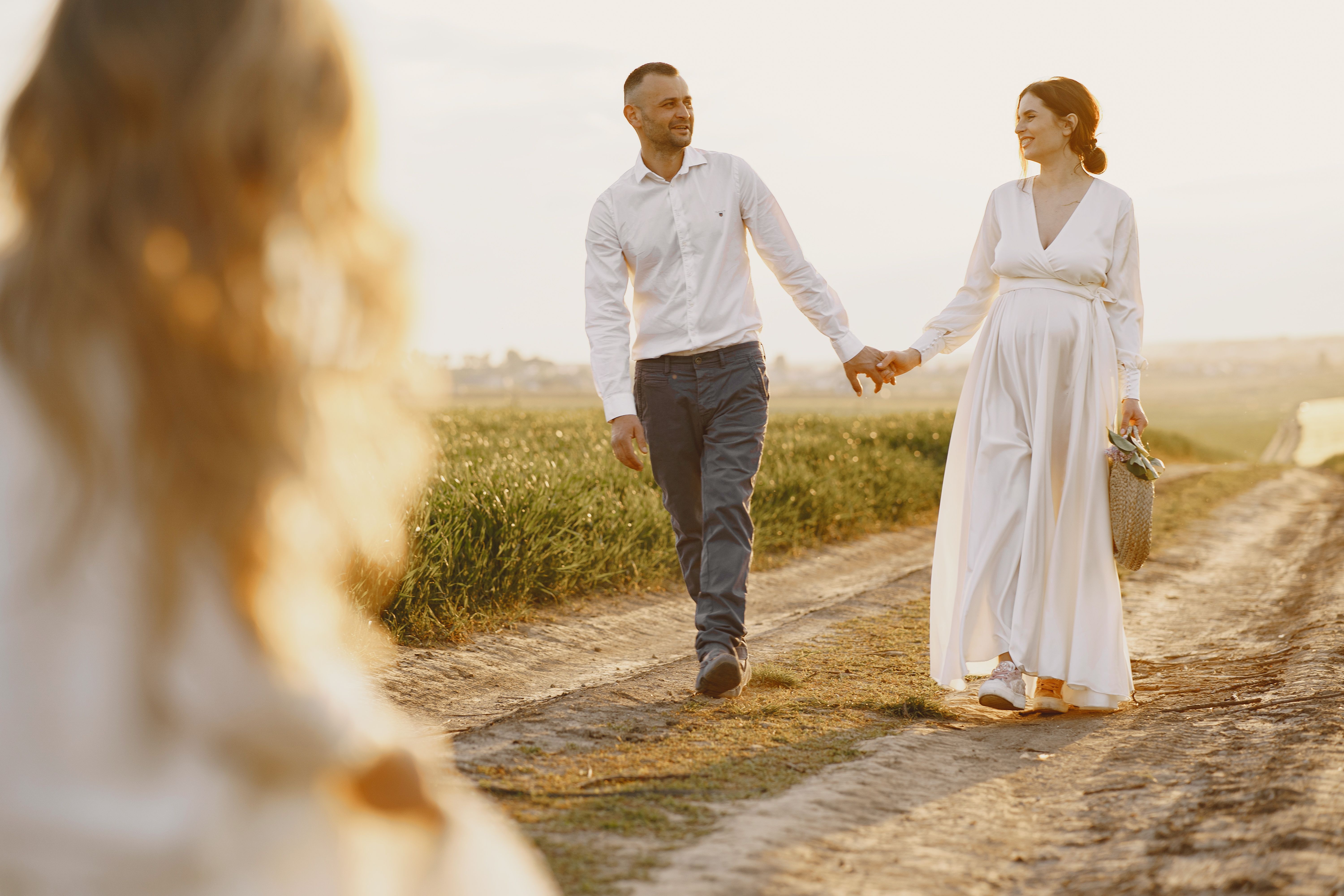 A couple holding hands, walking on a rural path at sunset, capturing a romantic and serene moment.
