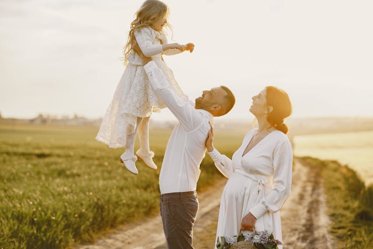 Family Dressed In White Elegant Clothes Standing In Rural Landscape In A Morning Sunlight