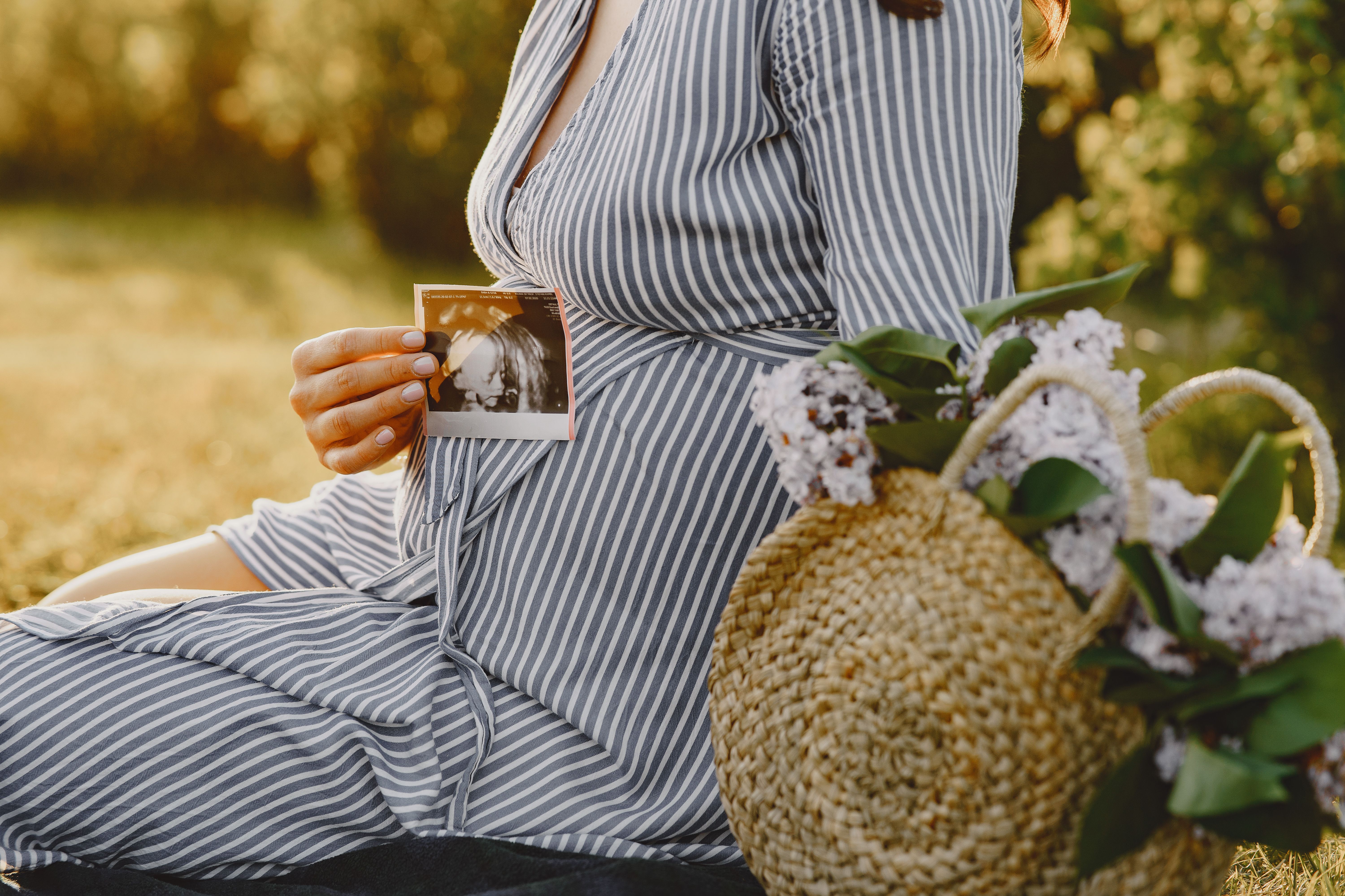 Pregnant woman sitting outdoors holding a sonogram, showcasing maternal anticipation and joy.