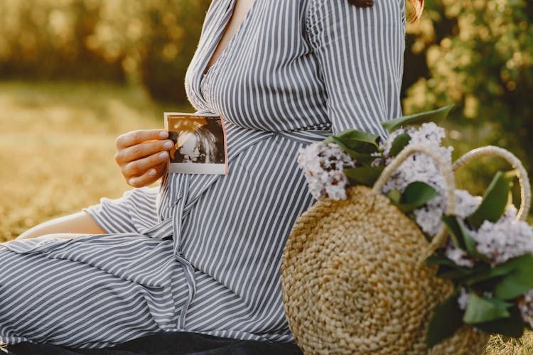 A Woman Holding A Sonogram Next To Her Belly