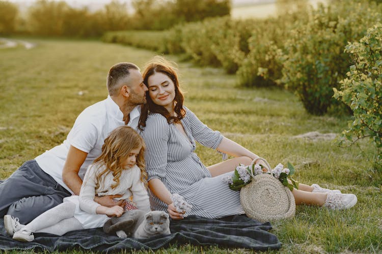 A Family With A Cat Sitting On Green Grass