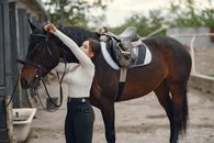 Woman in White Long Sleeve Shirt and Black Pants Standing Beside Brown Horse
