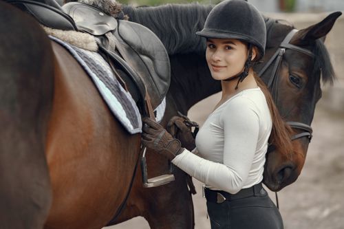 Free Smiling woman equestrian standing beside her horse wearing a helmet outdoors. Stock Photo