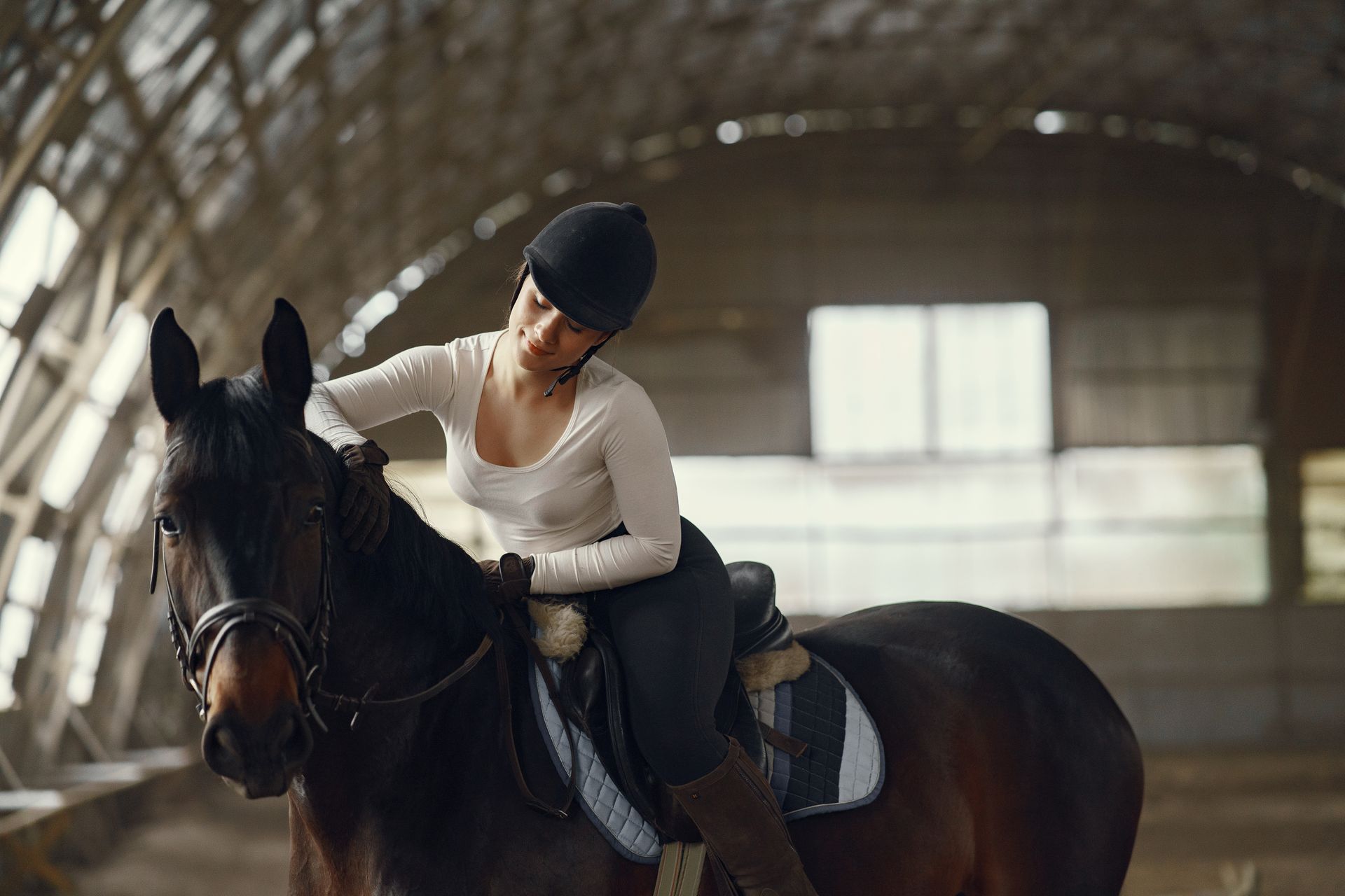 A woman riding a horse in an indoor equestrian arena, wearing a helmet.