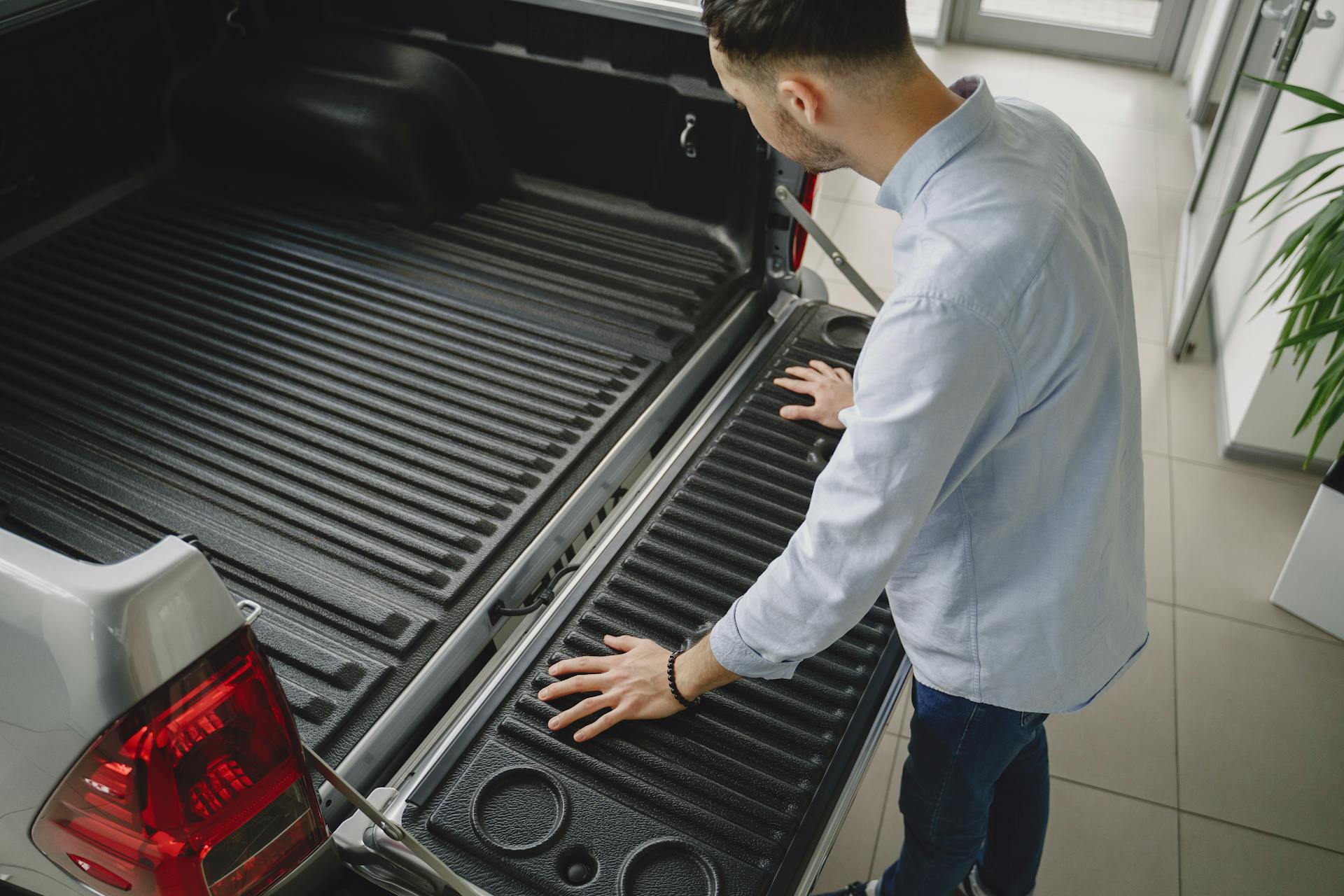 Adult man examines tailgate of a new pickup truck in a vehicle showroom.