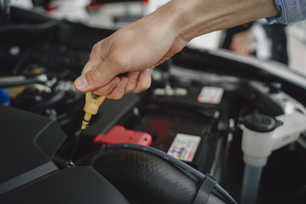 Hand checking oil dipstick in a car engine bay during routine maintenance. Photo by Gustavo Fring on Pexels.