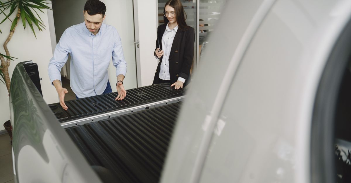 Salesman and client inspecting a pickup truck in a car dealership, discussing features.