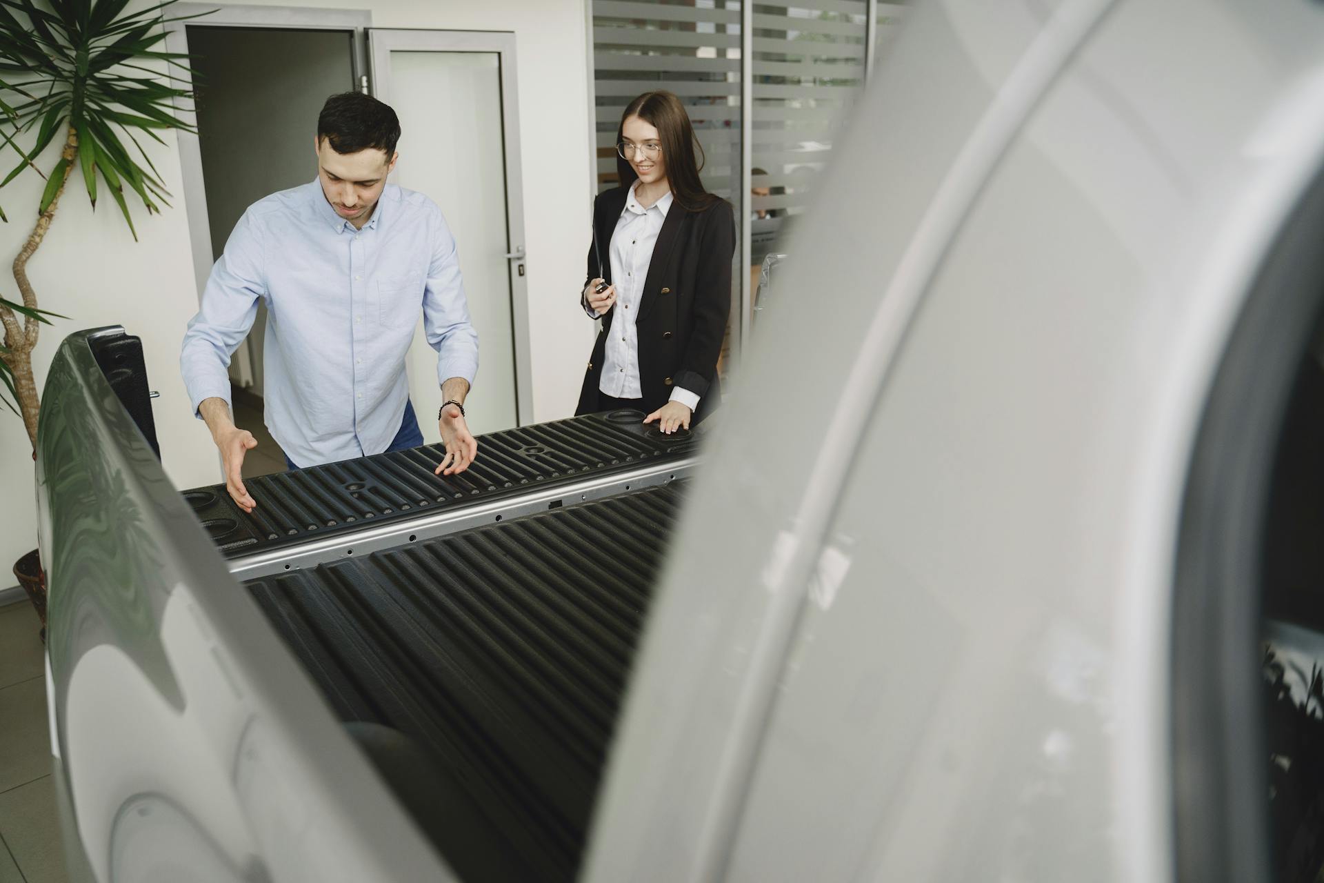 Salesman and client inspecting a pickup truck in a car dealership, discussing features.