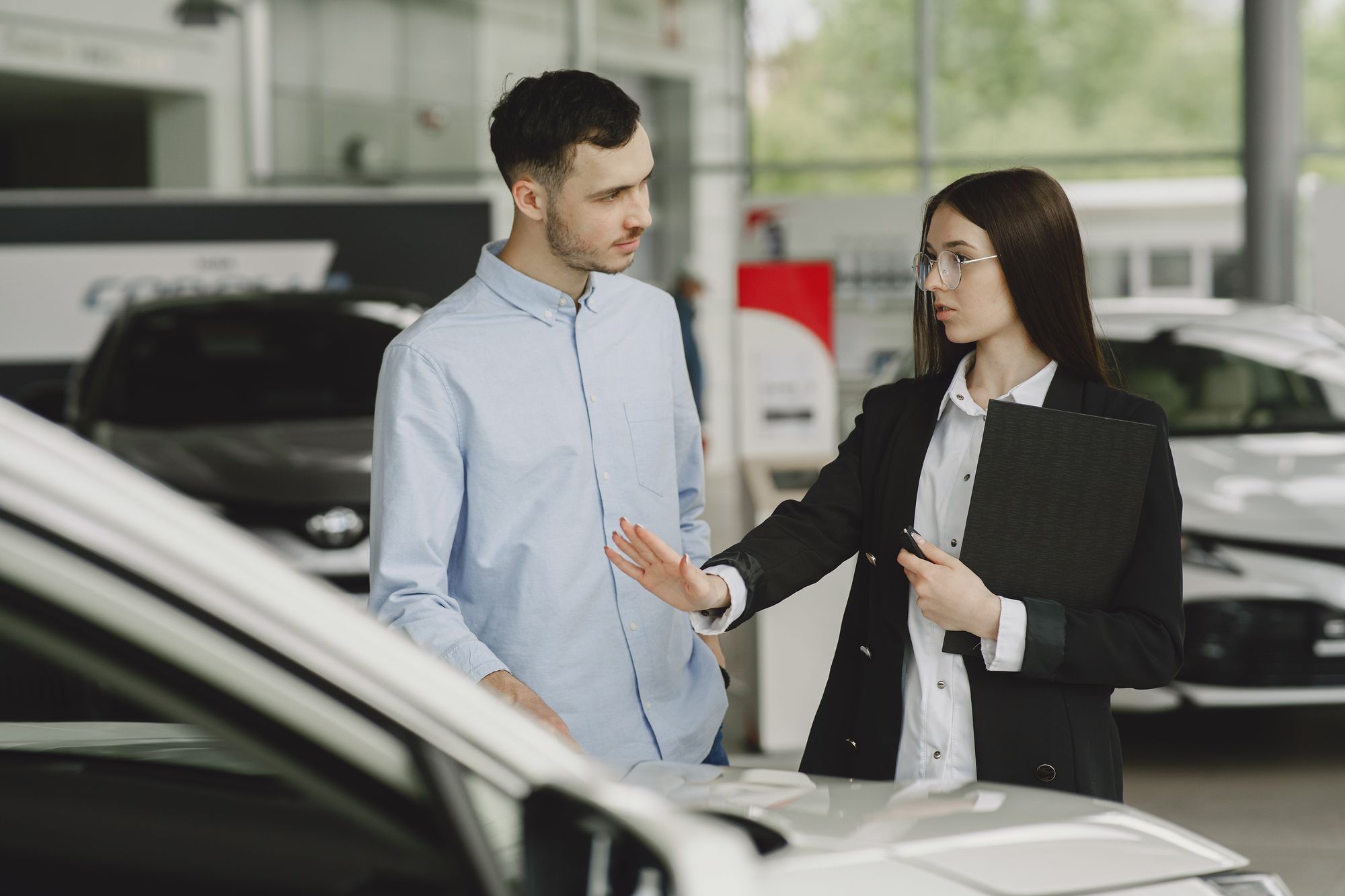 Shows a customer and salesperson in a dealership discussing a deal, directly matching the article