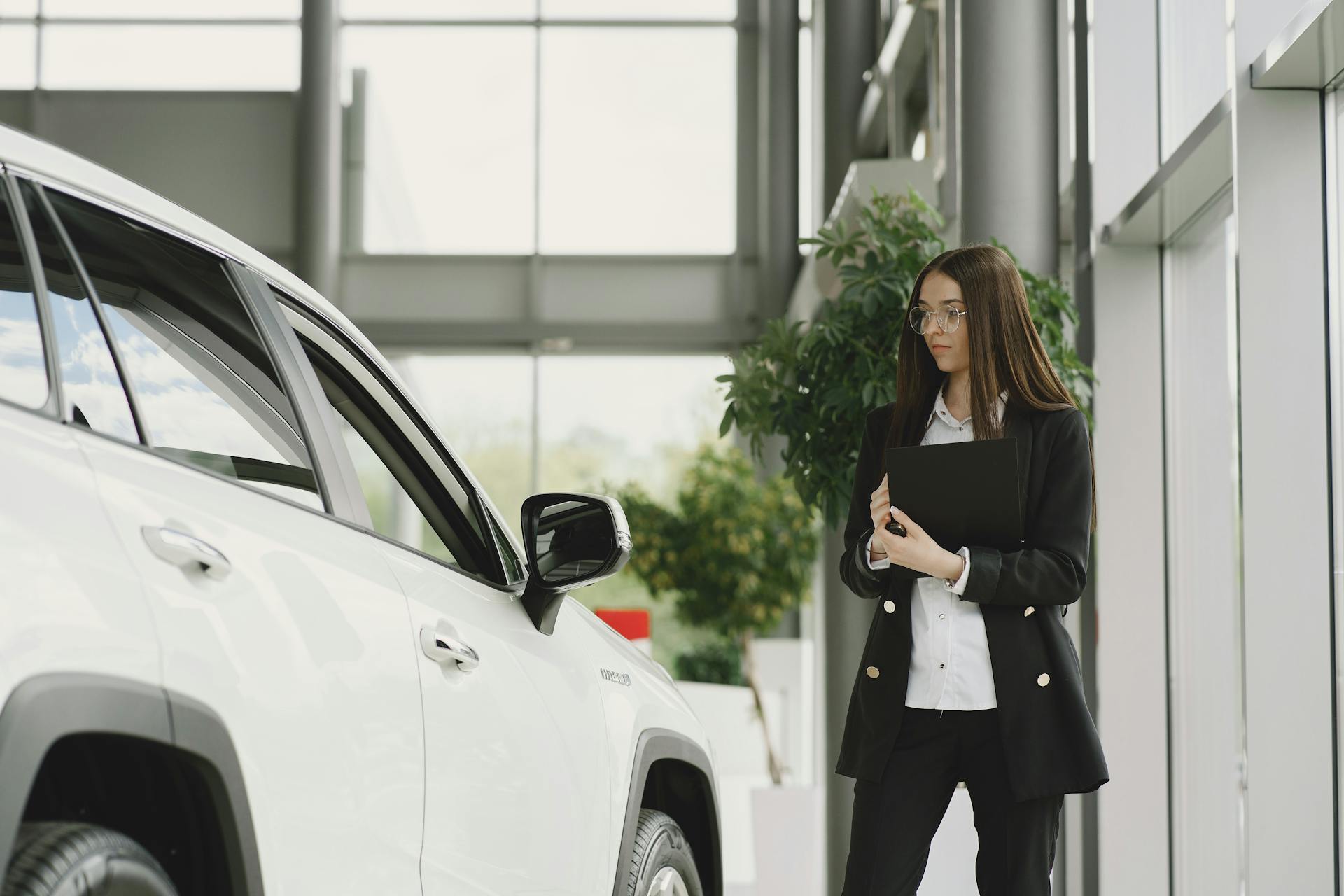 A businesswoman examines a luxurious vehicle inside a sleek, modern car dealership showroom.