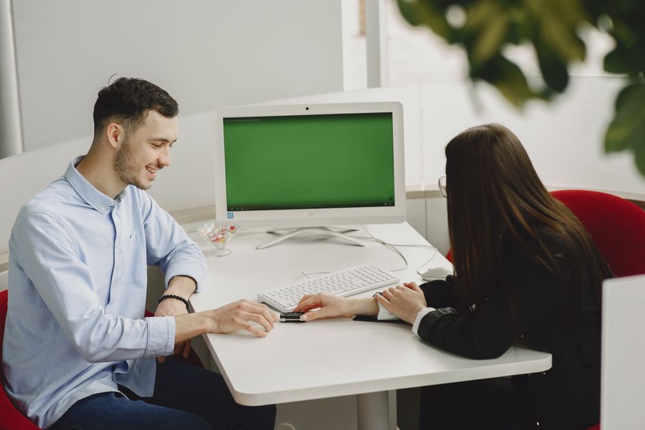 A man and woman collaborate in a modern office space with a desktop computer.