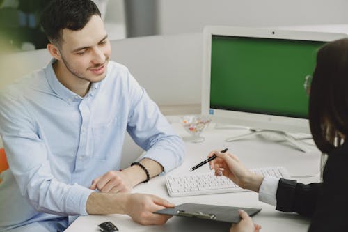 Employees Sitting by Desk Discussing Work 