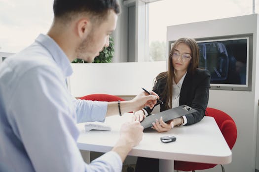 A man and woman discussing and signing a document at a table in an office setting.