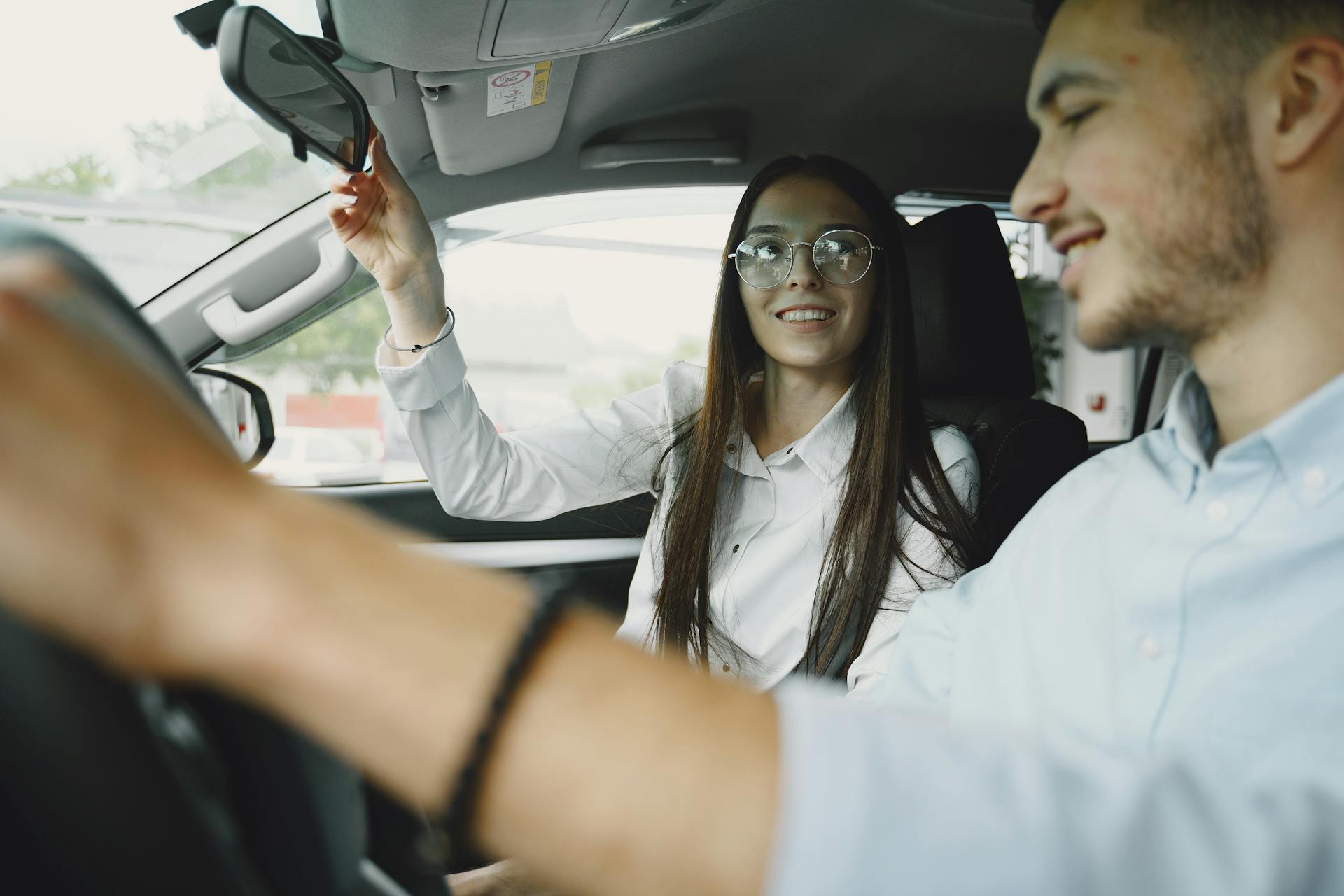 A cheerful young couple driving with focus on woman adjusting the mirror.