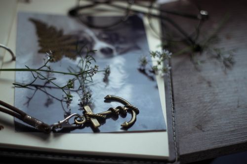 Free Composition of decorative anchor styled pendant placed on opened diary near eyeglasses and tiny white flowers Stock Photo