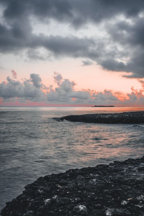 Free Spectacular scenery of rippling surface of ocean with rough rocky coast under bright cloudy sky at sunset Stock Photo