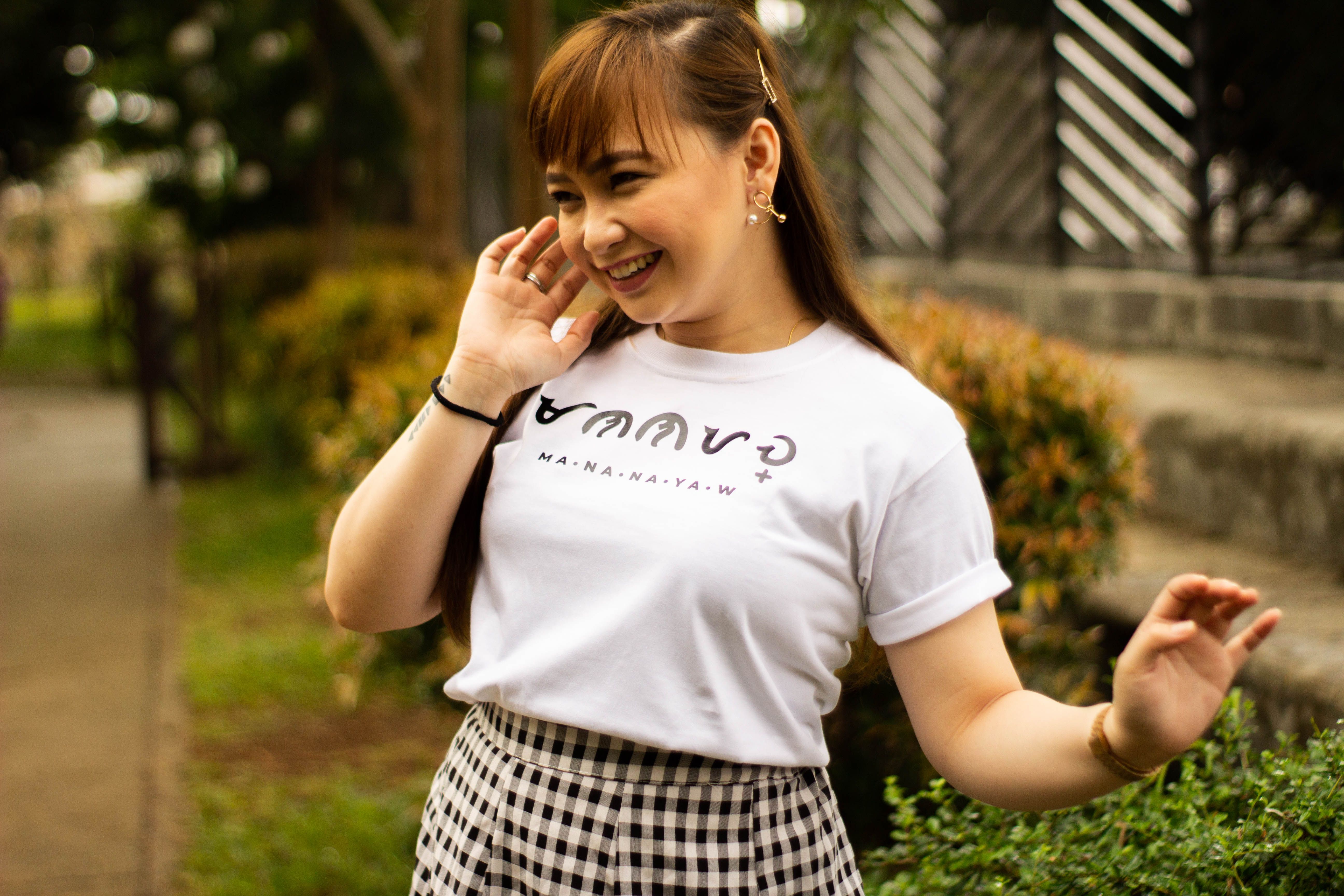 Cheerful woman in a park wearing a casual t-shirt and checkered skirt.