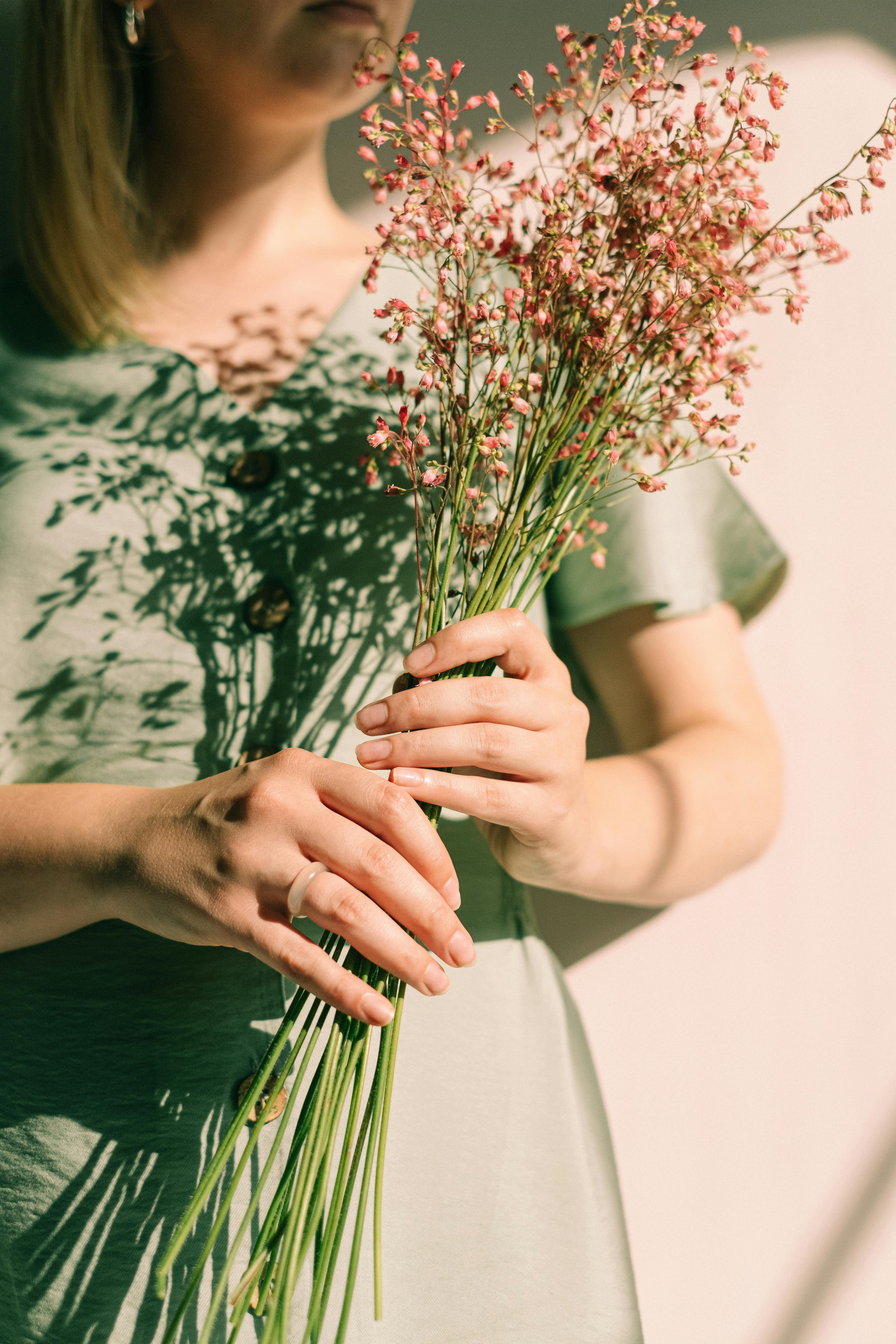 Woman in green dress holding a bouquet of pink flowers, highlighted by sunlit shadows.