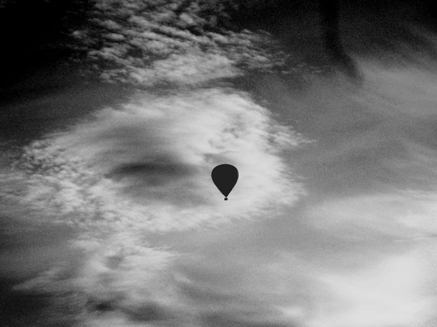 A grayscale image featuring a silhouette of a hot air balloon against a dramatic cloudy sky.
