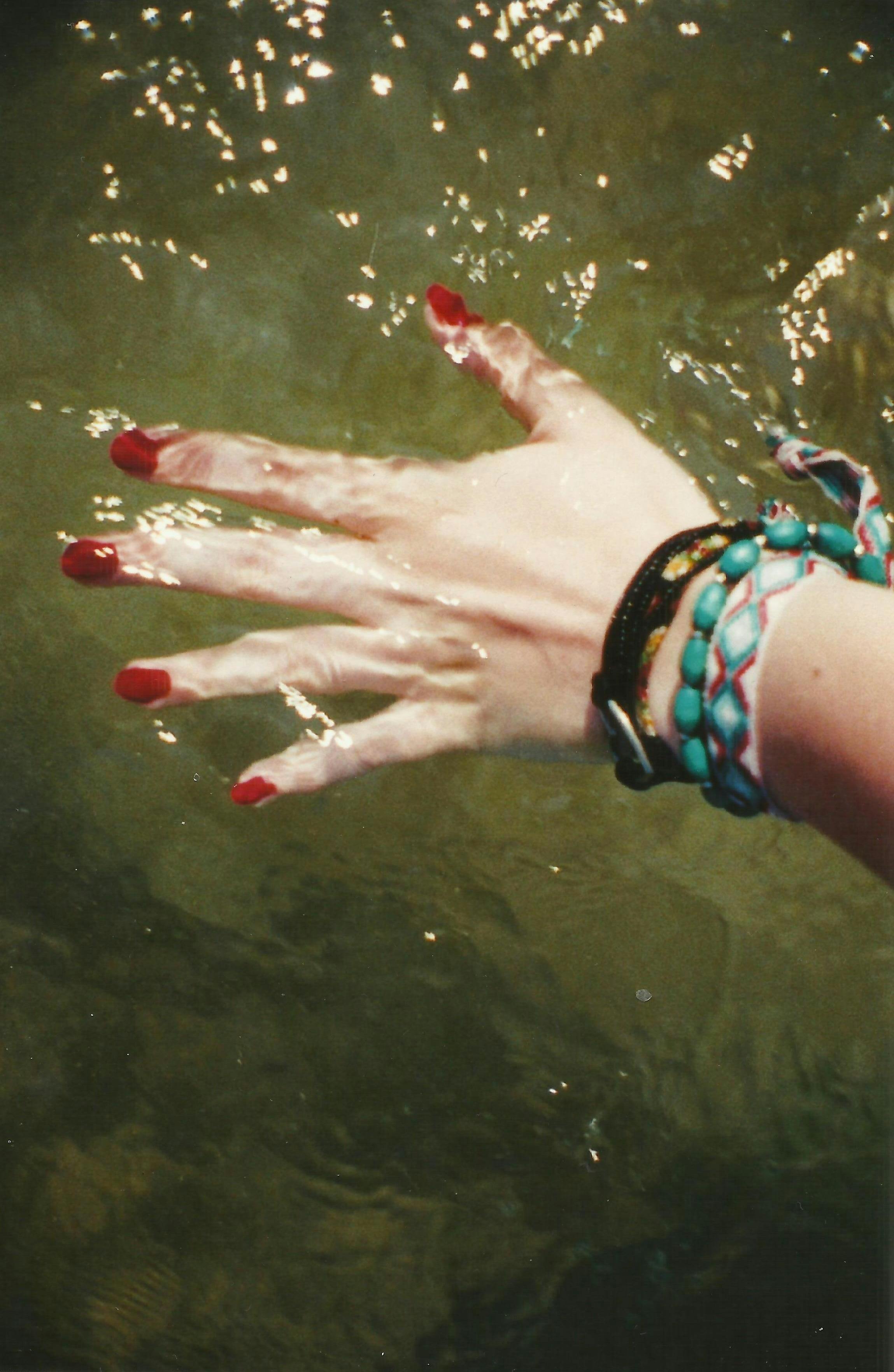 Hand with manicured nails and bracelets touching sparkling water, creating a serene effect.