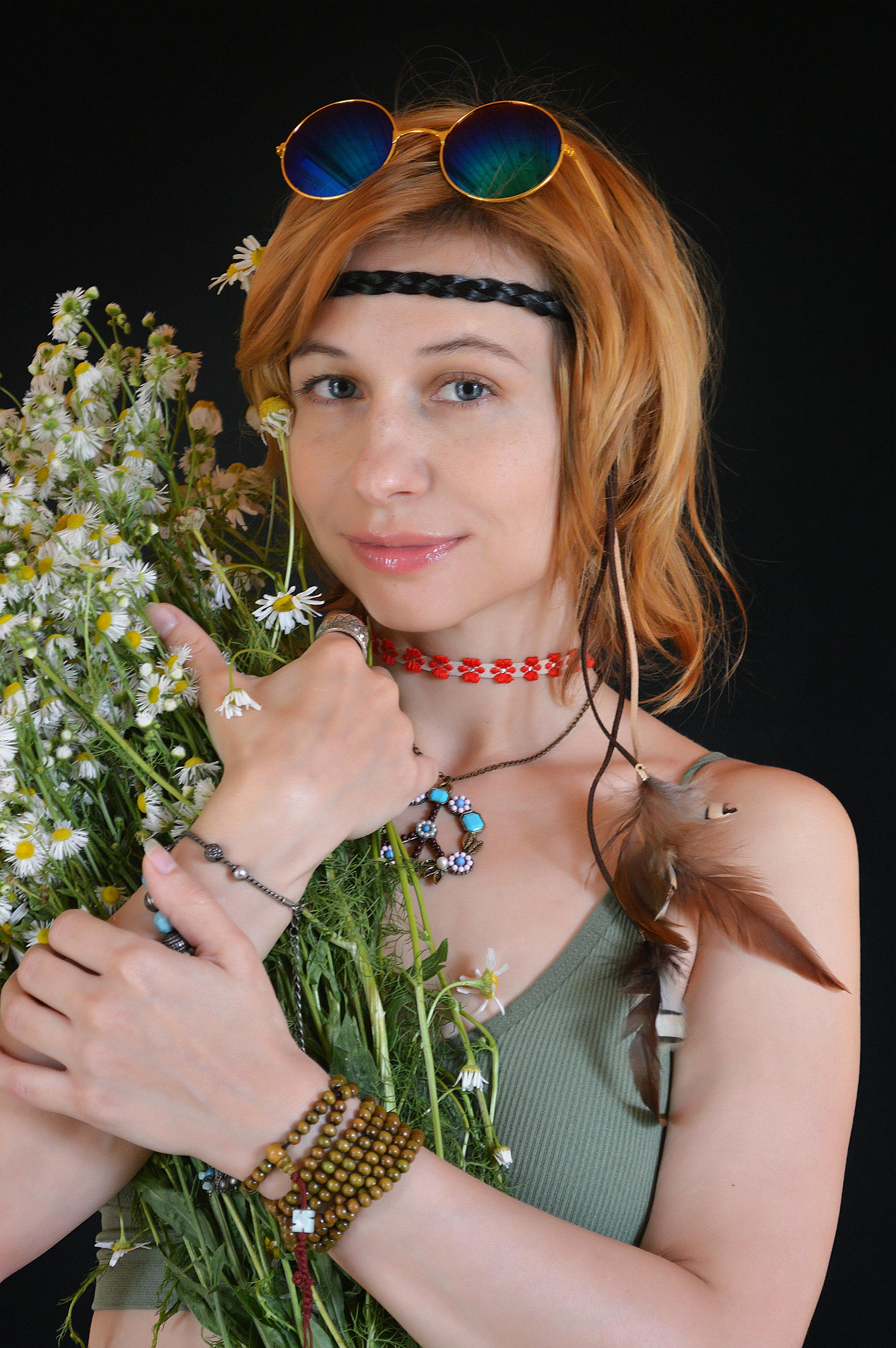 一位面带微笑的年轻女性，手捧一束新鲜的雏菊，注视着黑色背景的镜头