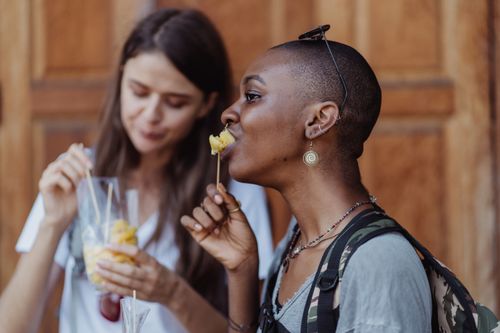 Free Two women savoring fruit skewers outdoors, capturing a moment of enjoyment and hunger satisfaction. Stock Photo